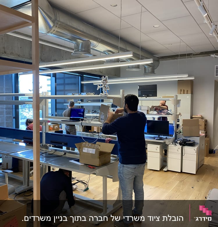 אנשים מסדרים ציוד משרדי ומחשבים במשרד חדש